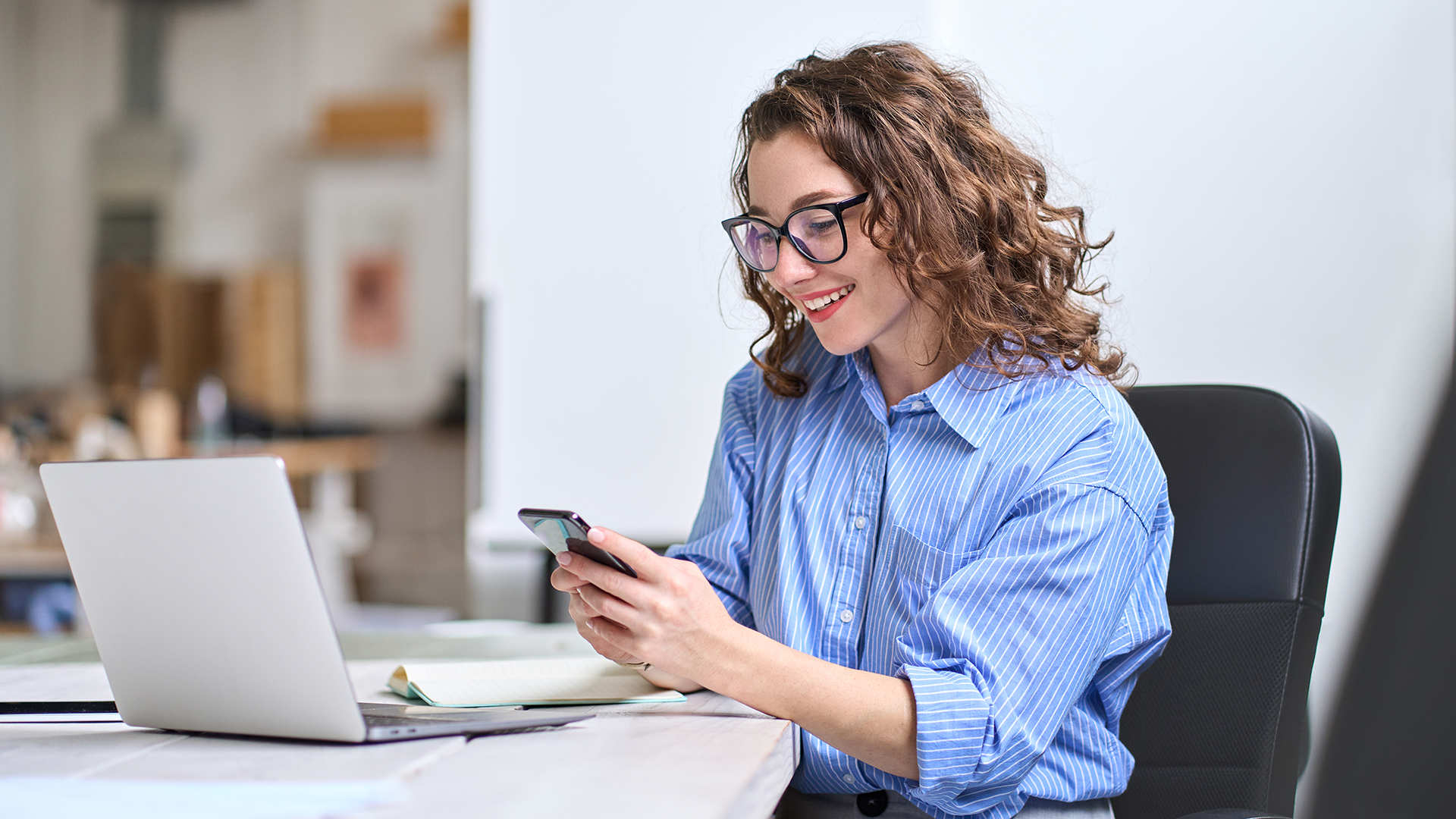 Woman looking at her phone next to a laptop