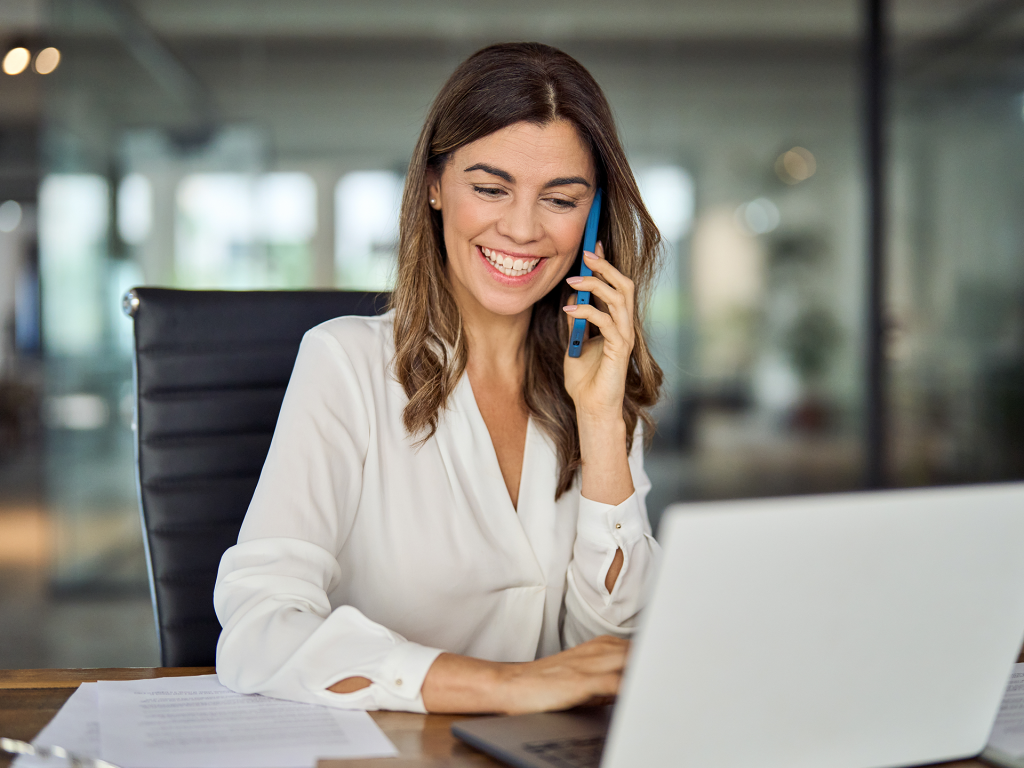 A woman talking on a phone while typing on a computer. Representing Contact IQ's internal routing features.